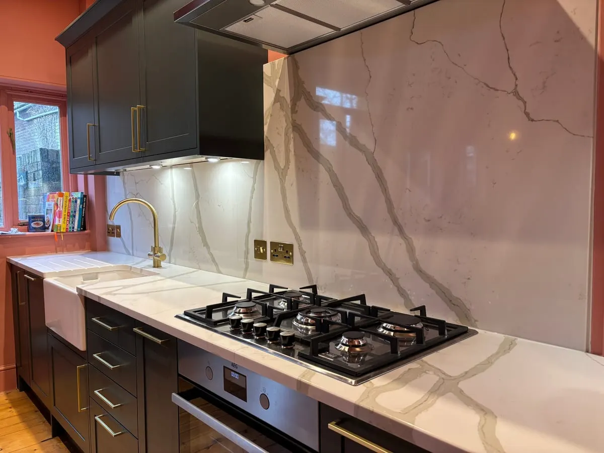 Marble and Brass Shaker Kitchen Dark shaker kitchen with veined marble worktop and splashback, gas hob, brass tap and butler sink